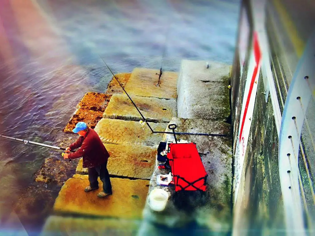 Pescador segurando diferentes tipos de varas de pesca, pensativo sobre qual escolher.