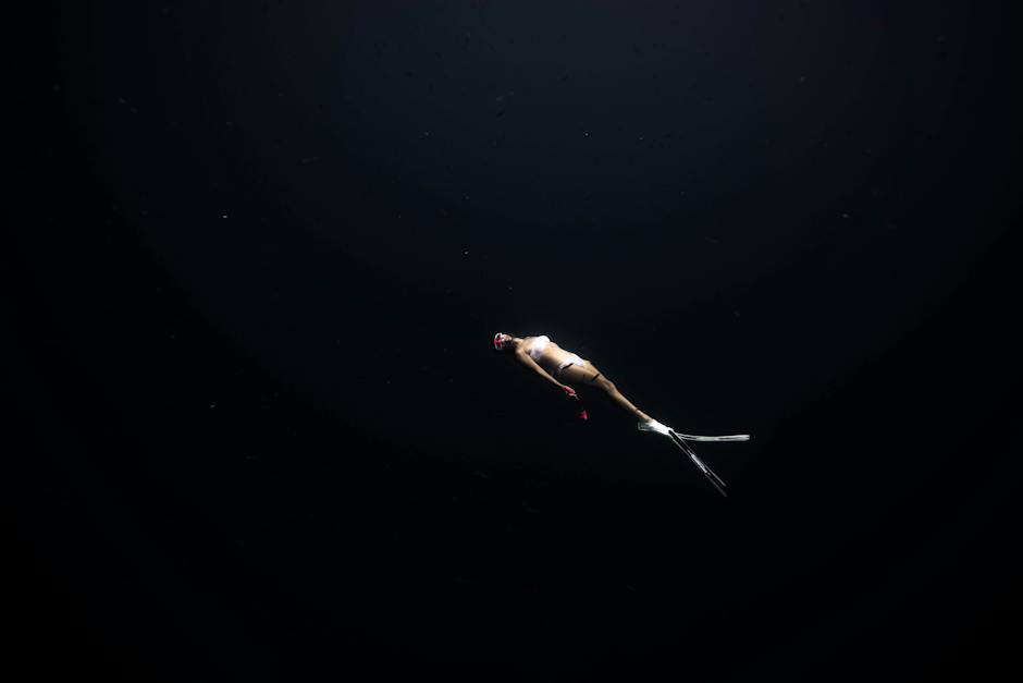 Image of a person diving underwater at night with a fishing spear in hand