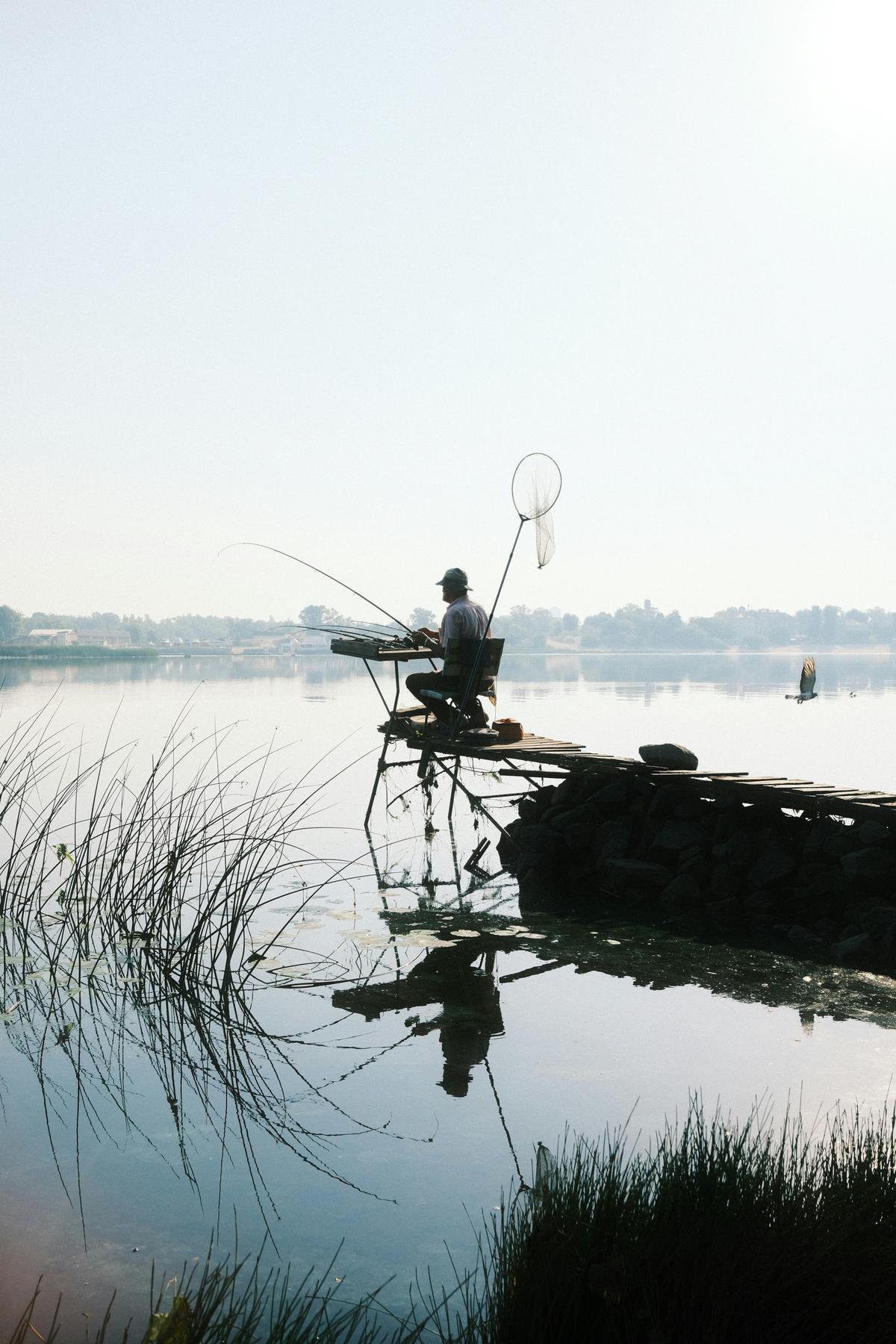 Pescador iscando um anzol com uma minhoca, sentado à beira de um rio ou lago