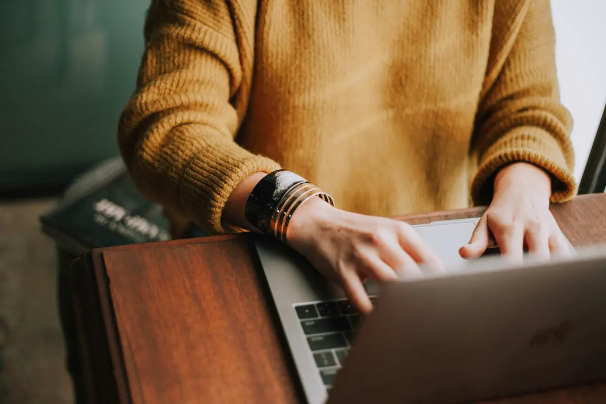 Uma pessoa usando um computador para fazer compras online, com foco nas mãos digitando no teclado e na tela mostrando um site de comércio eletrônico